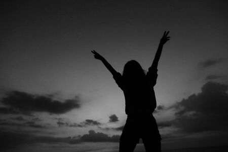 Black female silhouette with raised hands on grey sunset sky background in Los Angeles. Concept of last minute tours to tropical resort, summer vacations and gladden tourist.の写真素材