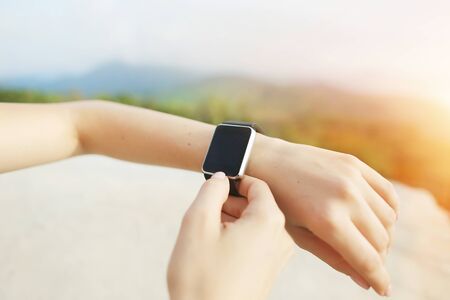 Sunny photo of closeup hands using smartwatch with mountains in background. Concept of modern technology, useful gadget and nature.の写真素材