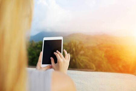 Sunshine photo of female person using tablet and taking photo of Thailand mountains. Concept of summer vacations, last minute tours and modern technology.の写真素材