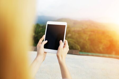 Bright photo with sunshine of blonde woman using tablet, mountains in background, Bali. Concept of tropical resort, modern technology and summer vacations.の写真素材