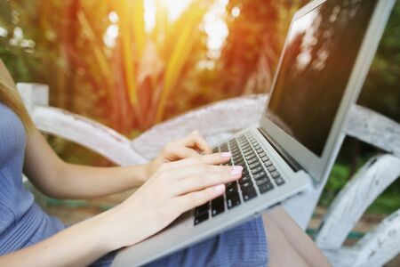 Concept of new technologies for better life, travel to tropical countries. close up woman hand fingers press laptop keyboard for freelancing remote work on sunny day, background of sunshine green palms in Thailand, Phuket.の写真素材