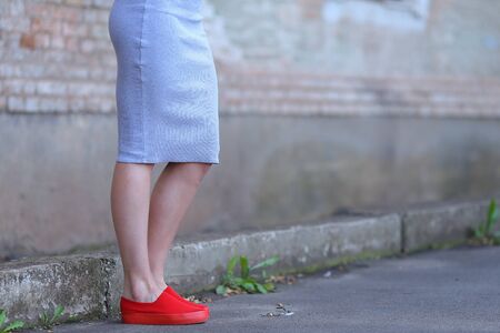 Legs girl in red slip-on, one leg bent at knee on background of gray concrete wall of stone. Concept of advertising footwear slipony, comfortable shoes.の写真素材