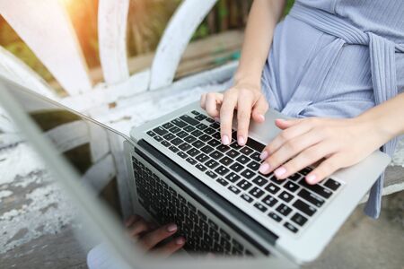 above portrait close up woman hand fingers press laptop keyboard for freelancing remote work on sunny day, background of sunshine green palms in Thailand, Phuket. Concept of new technologies for better life, travel to tropical countriesの写真素材