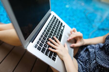 woman and kid Fingers typing on the computer keyboard. Close up portrait of two hands pressing buttons on laptop at sunny day swimming pool. concept of business freelance working, new technologiesの写真素材