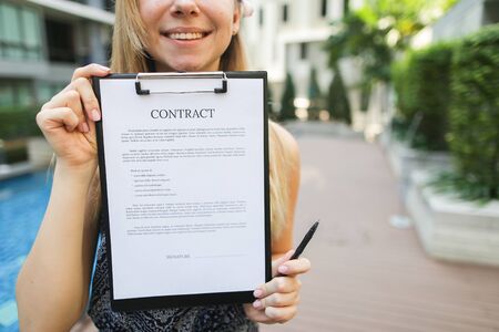 young pretty woman offer to sign contract on background of new apartment building. concept of long term rent of car, condo or traveling. Front used with Open Font Licenseの写真素材