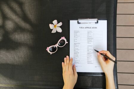 bright flat lay of woman hands fill visa application with pen for travel, sunlight portrait with sunglasses and flower. concept of traveling journey. Front used with Open Font Licenseの写真素材