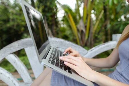 Female person using laptop, palms in background. Concept of exotic summer vacations and modern technology.の写真素材