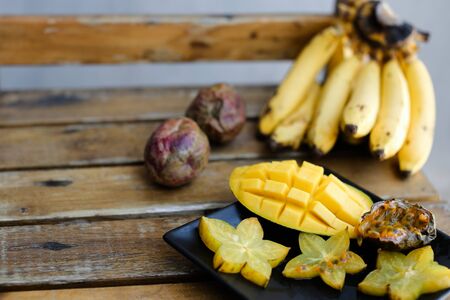 Close up tasty mango and carambola on plate near bananas on wooden table. Concept of tropical fruits and exotic healthy food.の写真素材
