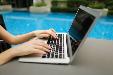 concept of business freelance working, new technologies. Fingers typing on the computer keyboard. Close up portrait of woman hands pressing buttons on laptop at sunny day swimming pool.の写真素材