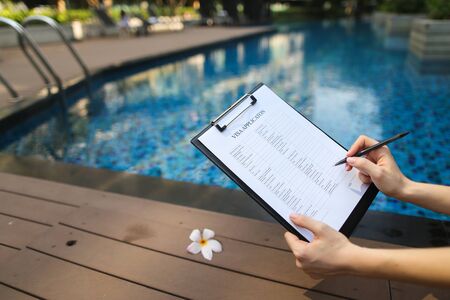 Girl holding empty document, Focus on paper. young businessman signs important documents on vacation on pool background. concept of remote work, freelancing on sunny day. Front used with Open Font Licenseの写真素材