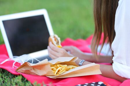female in the park works behind laptop. beautiful girl with glasses eating fast food in nature and smiling.の写真素材