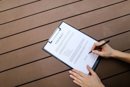 beautiful flat lay of young woman hands with pen sign contract, wooden backgroung. concept of business work agreement, freelance working remotely. Front used with Open Font Licenseの写真素材