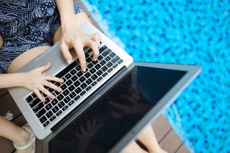 Family Fingers typing on the computer keyboard. Close up portrait of woman and little girl hands pressing buttons on laptop at sunny day swimming pool. concept of business freelance working, new technologiesの写真素材