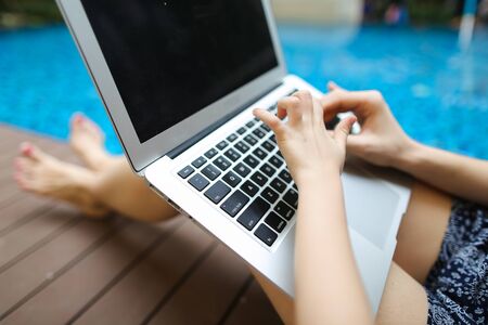 mother and daughter Fingers typing on the computer keyboard. concept of business freelance working, new technologies. Close up portrait of woman hands pressing buttons on laptop at sunny day swimming pool.の写真素材