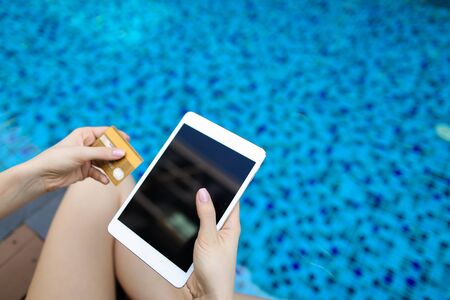 bright sunny portrait of young woman hands holding gold credit debit card and laptop on swimming pool background. Concept of online transfer payment, money exchangeの写真素材