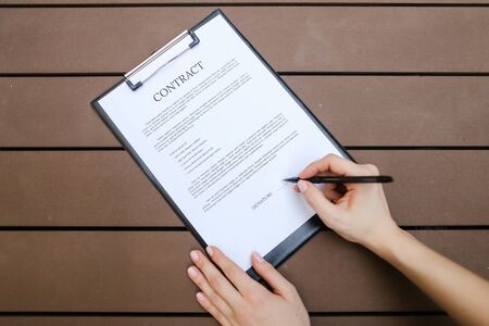 beautiful flat lay of young woman hands with pen sign contract, wooden backgroung. concept of business work agreement, freelance working remotely. Front used with Open Font Licenseの写真素材