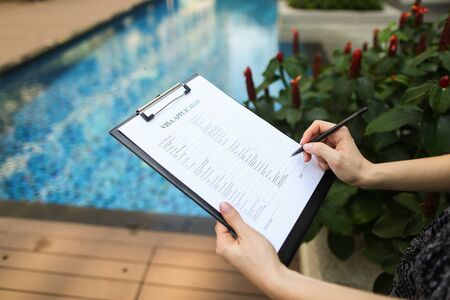 large portrait of woman's hand fills out application form for Iceland against pool background. concept of long-term travel to warm countries. Front used with Open Font Licenseの写真素材