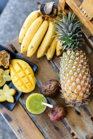 Kiwi fresh green juice near bananas, carambola with mango and pine-apple on wooden chair. Concept of exotic fruits and healthy tropical food.の写真素材
