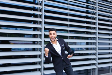 Young handsome businessman Arab Muslims is in the business center in black elegant dress on building background. Businessman man male looking waiting concept and smiling.の写真素材