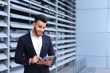 Young handsome businessman Arab Muslims is in the business center in black elegant dress on building background. Businessman man male looking waiting concept and smiling.の写真素材