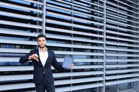 Young handsome businessman Arab Muslims is in the business center in black elegant dress on building background. Businessman man male looking waiting concept and smiling.の写真素材