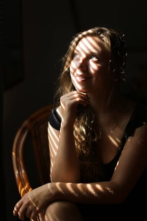Portrait of young pretty woman sitting in chair, striped shadows. Concept of female beauty and home photo session.の写真素材
