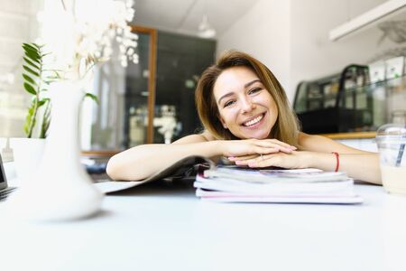 Young smiling girl sittting at cafe and reading magazins. Concept of learning and having break, student life.の写真素材