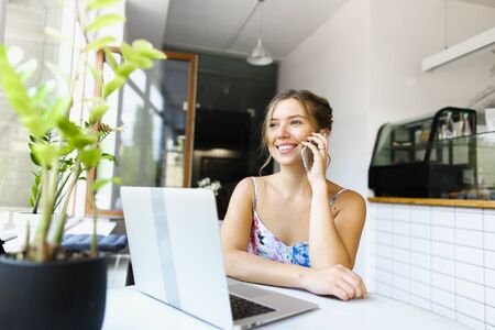Pretty american woman speaking by smartphone and using laptop at cafe. Concept of booking tour online.の写真素材