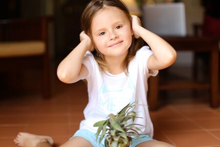 Portrait of little female barefoot kid sitting on floor with pineapple. Concept of fruits and...