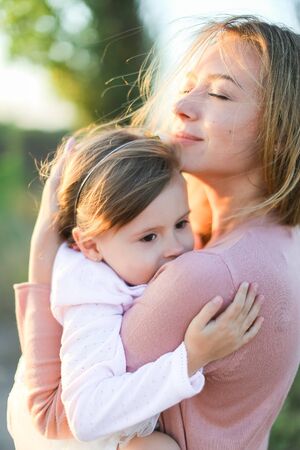 Young blonde woman hugging little daughter and smiling. Concept of family portrait and motherhood.