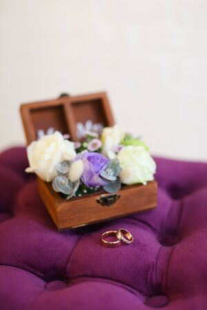 Two golden rings on violet pillow near box with flowers. Concept of wedding jewelry.