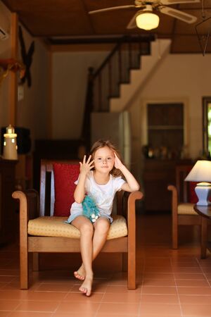 Little female kid sitting in chair with in living room. Concept of leisure time for children and wooden interior.の写真素材
