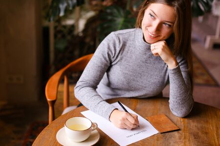 Young caucasian woman filling visa application, passport and cup on table. Concept of travel agency and emigration.の写真素材