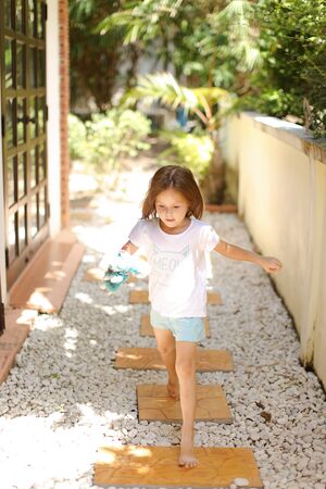 Little caucasian female kid walking barefoot on white gravel near exotic hotel. Concept of vacation with kid in Thailand, Phuket.の写真素材