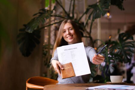 Focus on visa aplication, pen and passport in young woman hands at travel agency cabinet. Concept of execution of document for emigration.の写真素材