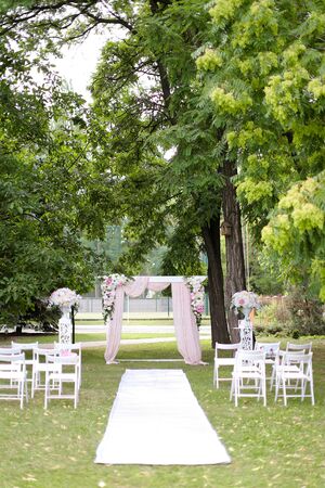 Decorated expensive wedding arch decorated by flowers and chairs in park. Concept of marriage ceremony place and photo session in open air.の写真素材
