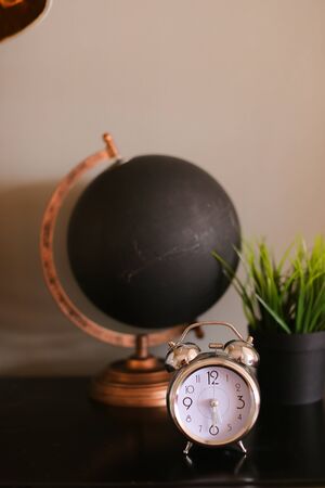 Black matte decorative stylish globe an alarm clock standing on table near houseplant. Concept of geography cabinet and tourist agency.の写真素材