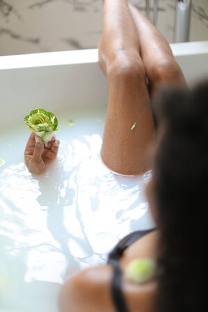 Focus on flower, back view afro american woman taking milk bath and wearing bra. Concept of spa and aromatherapy.の写真素材