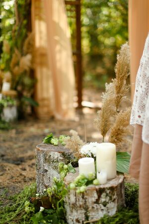 White paraffin candles on wood stumps near wedding altar or arch. Concept of handmade wedding decorations.の写真素材