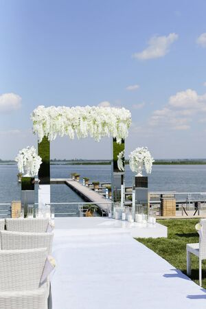 White amazing wedding altar decorated by flowers with lake in backround. Concept of bridal outdoor ceremony place.の写真素材