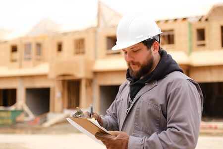 Male caucasian engineer drawing plan in notebook at construction site and wearing hardhat. Concept of architectural profession and house building.の写真素材
