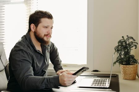 Caucasian financial analyst using smatrphone and laptop working at office. Concept of finances and business worker, modern technology.の写真素材