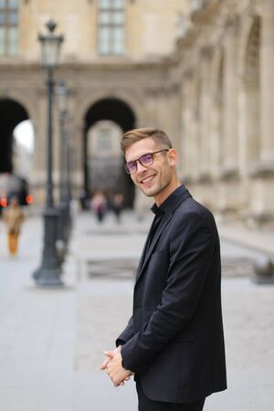 Young man standing near building in city and wearing black suit, lanterns in background. Concept of male fashion model and urban photo session.の写真素材