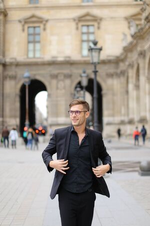 Young man in glasses walking in Paris and wearing black suit, France. Concept of walking in city and male fashion.の写真素材