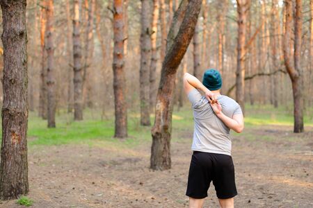 Back view of young boy doing morning exercises in park. Concept of workout and health. Man resting in spring forest.の写真素材