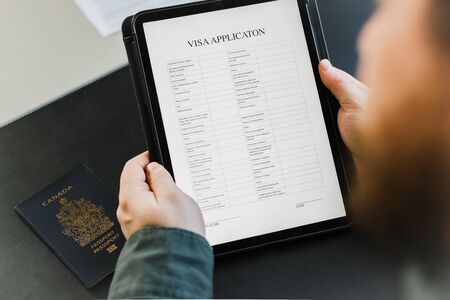 Close up businessman getting visa and reading application on tablet, passport on desk at office. Concept of migration, business trip and traveling.の写真素材