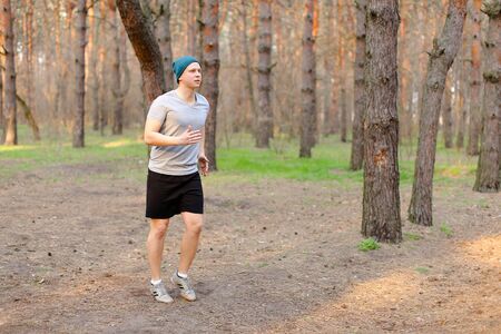 Young man jogging and running in morning park. Concept of fitness and health. Guy wearing cap and grey t shirt resting in spring forest.の写真素材