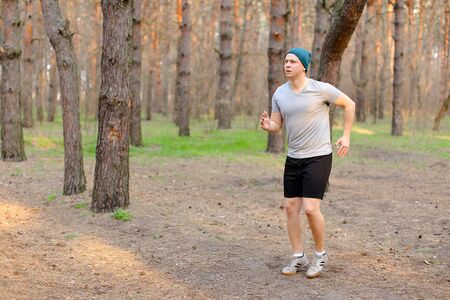 Young man jogging and running in morning park on fresh air. Concept of fitness and health. Guy wearing cap and grey t shirt resting in spring forest.の写真素材