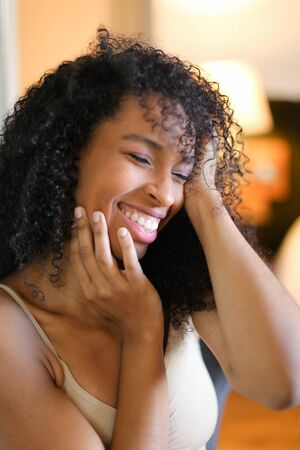 Portrait of young smiling afro american woman sitting in room and wearing beige swimsuit. Concept of hotel photo session in lingerie.の写真素材