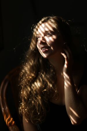 Portrait of american european woman sitting in chair, striped shadows. Concept of female beauty and home photo session.の写真素材